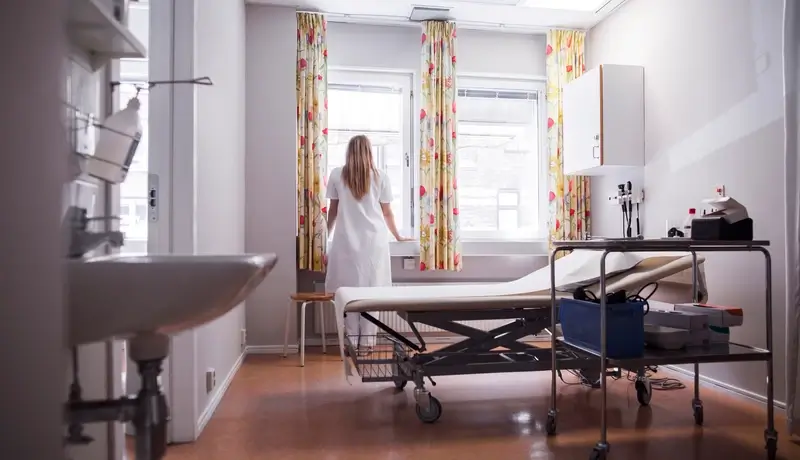 A private hospital room with a patient standing near the window, featuring a clean and peaceful environment.