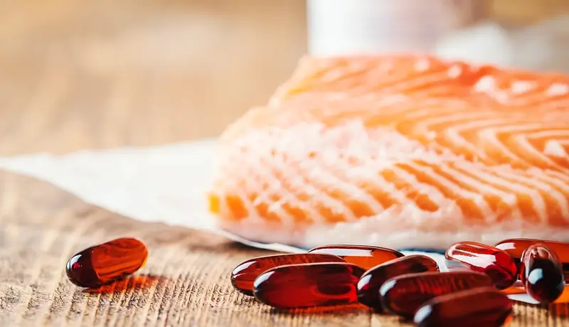 Fresh salmon and omega-3 supplement capsules placed on a wooden surface, highlighting their role in mental health support.