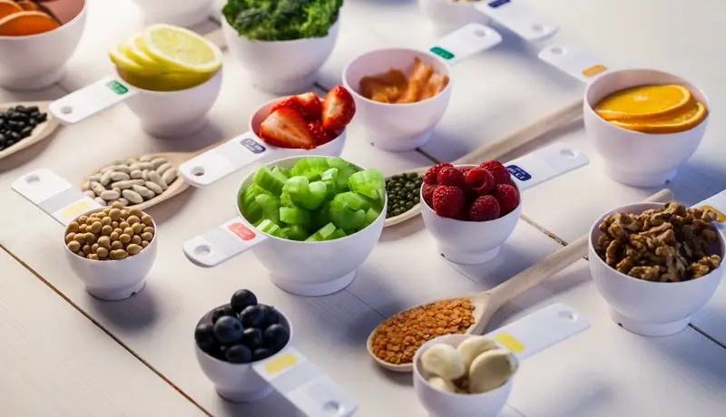 Various antioxidant-rich foods, including berries, nuts, greens, and citrus fruits, displayed in small bowls and measuring spoons.