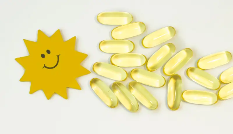 Vitamin D capsules arranged next to a smiling sun illustration, symbolizing the connection between sunlight and vitamin D benefits.