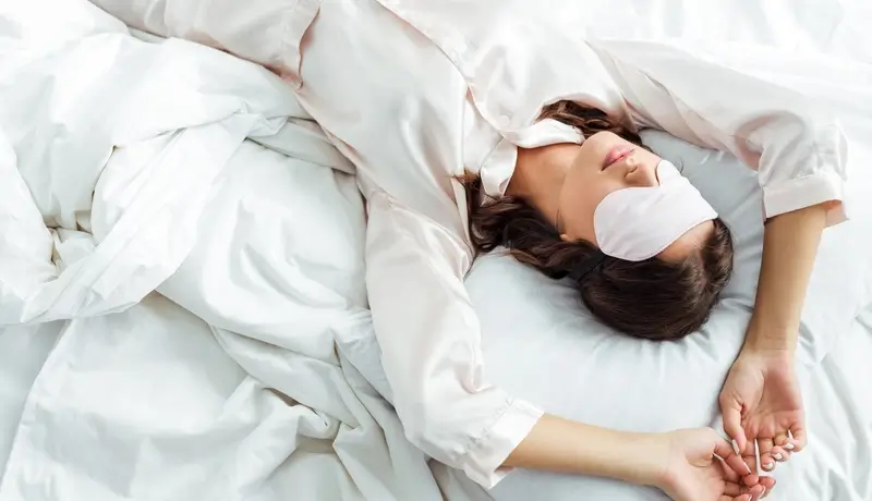 A woman sleeping peacefully in bed, wearing a sleep mask, symbolizing good sleep hygiene practices.