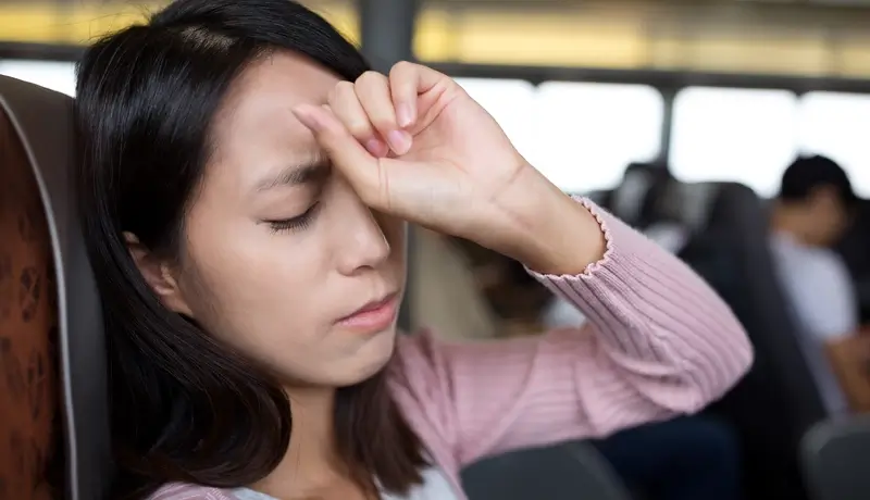 Woman holding her forehead, experiencing a headache while sitting on a bus.